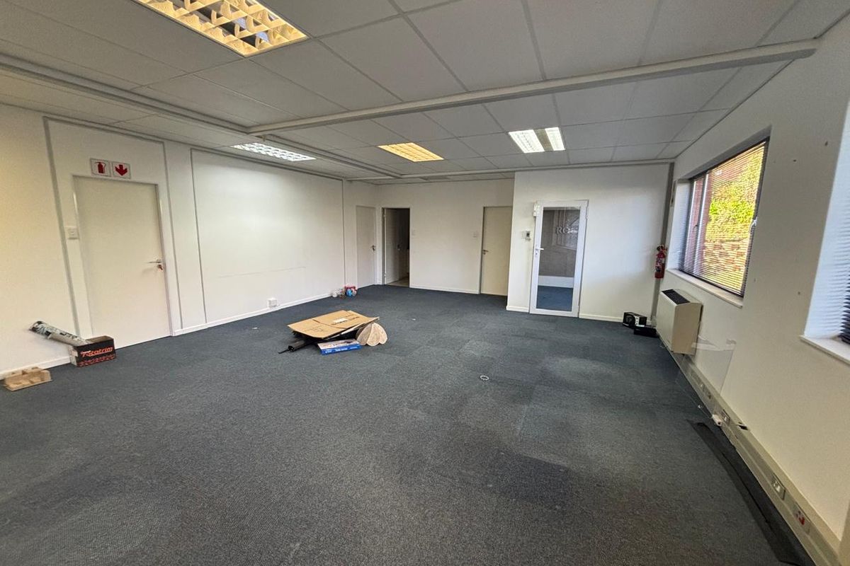 A spacious, empty office area featuring a suspended ceiling with recessed lighting, carpeted flooring, and an integrated air conditioning unit.