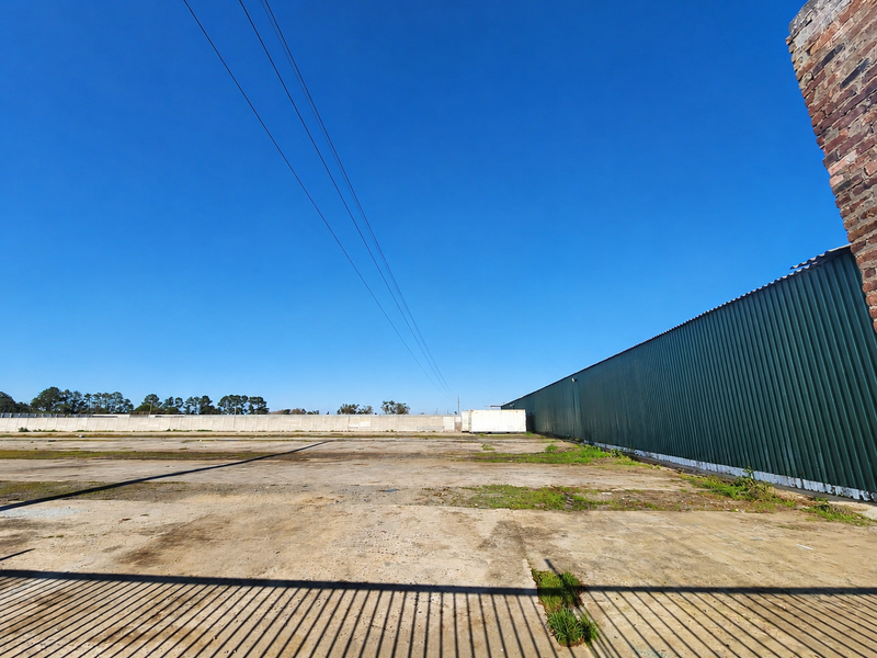 Expansive industrial yard featuring a large concrete surface, corrugated metal wall cladding, and secure precast concrete boundary walling.