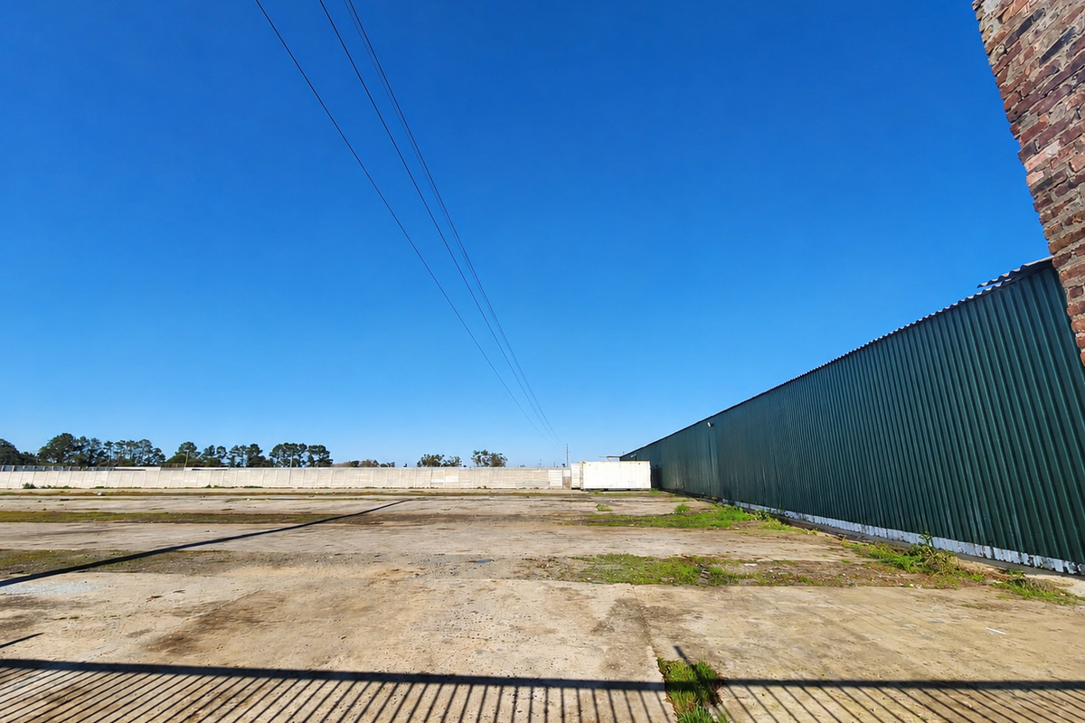 Expansive industrial yard featuring a large concrete surface, corrugated metal wall cladding, and secure precast concrete boundary walling.