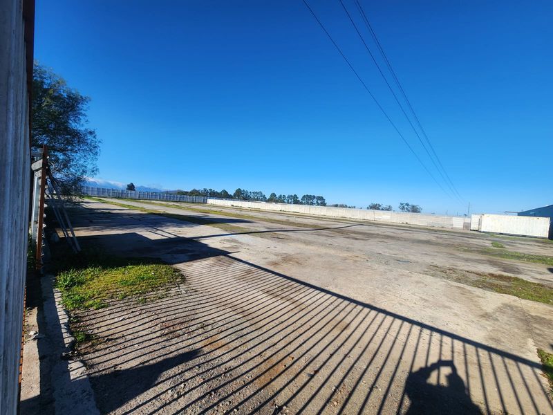 Expansive industrial concrete yard featuring perimeter walling and secure metal fencing, suitable for storage or logistics operations.