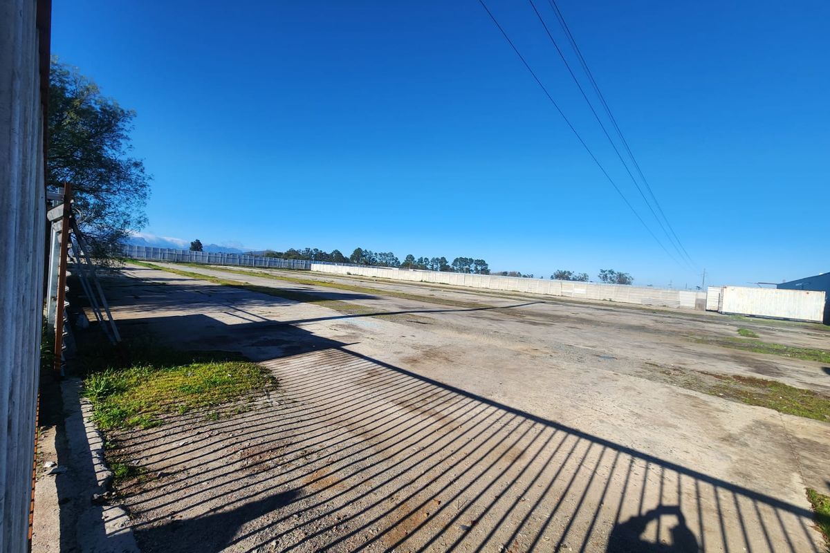 Expansive industrial concrete yard featuring perimeter walling and secure metal fencing, suitable for storage or logistics operations.