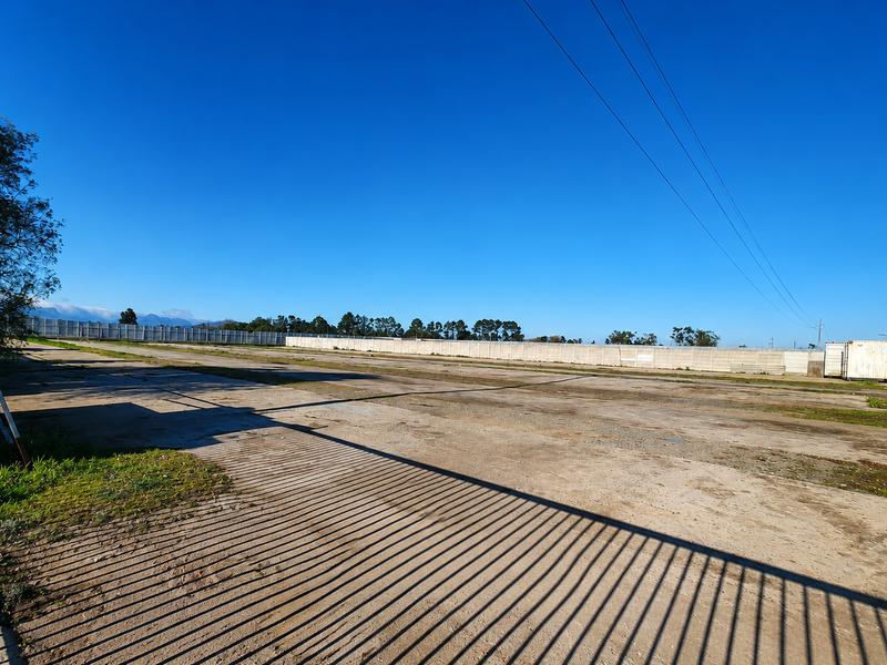 Expansive industrial concrete yard featuring a perimeter wall and a metal shipping container, suitable for storage or logistics operations.