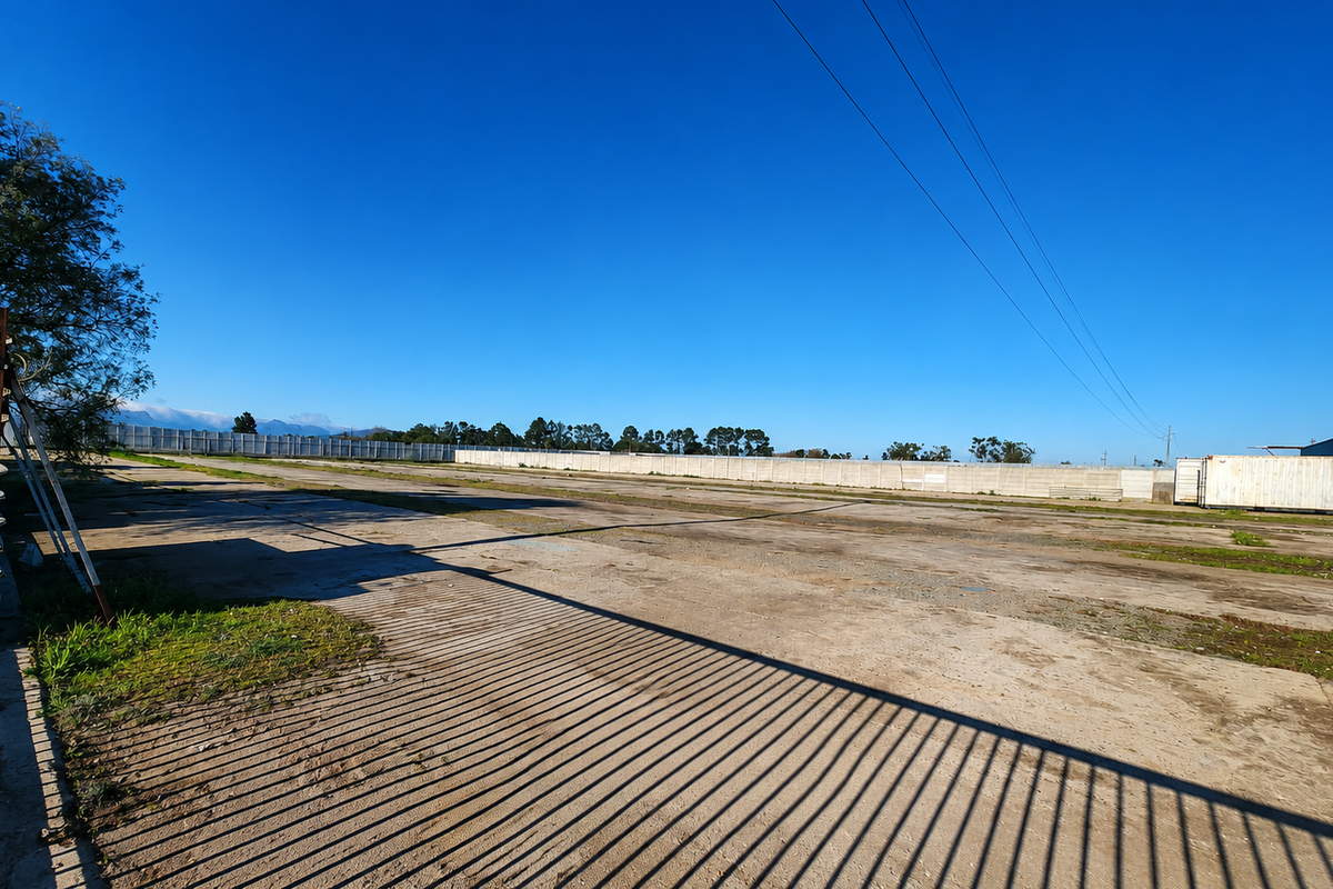 Expansive industrial concrete yard featuring a perimeter wall and a metal shipping container, suitable for storage or logistics operations.