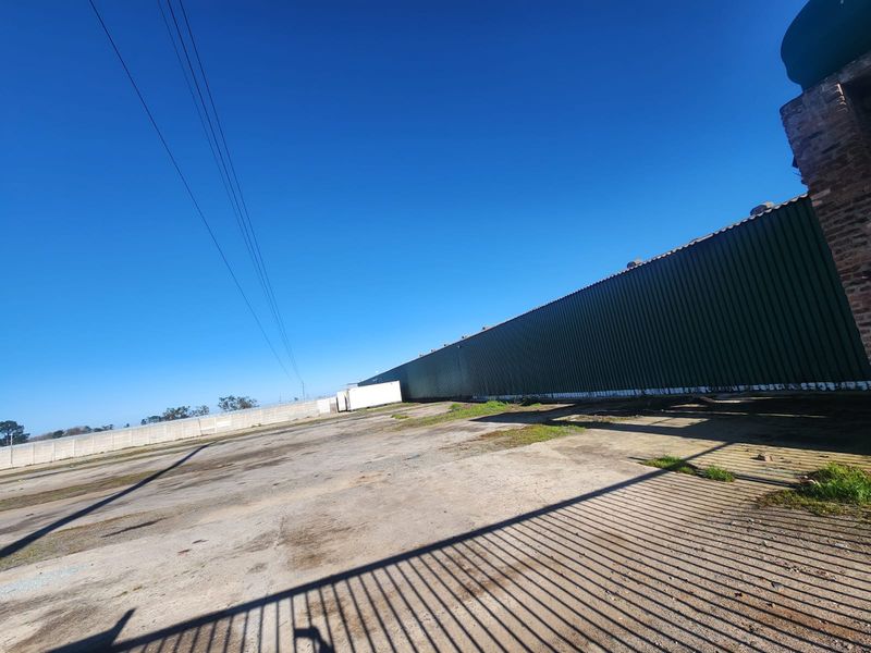 Expansive industrial yard featuring a large corrugated metal warehouse structure, concrete hardstand area, and perimeter security fencing.
