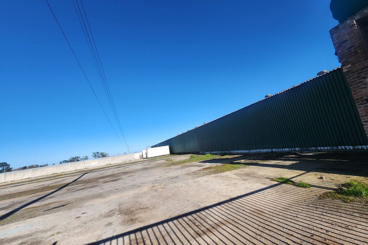 Expansive industrial yard featuring a large corrugated metal warehouse structure, concrete hardstand area, and perimeter security fencing.