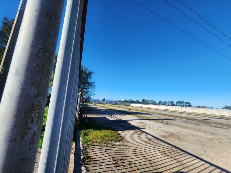 Expansive industrial yard area featuring concrete perimeter walls, metal security fencing, and paved ground surfaces suitable for storage or logistics operations.