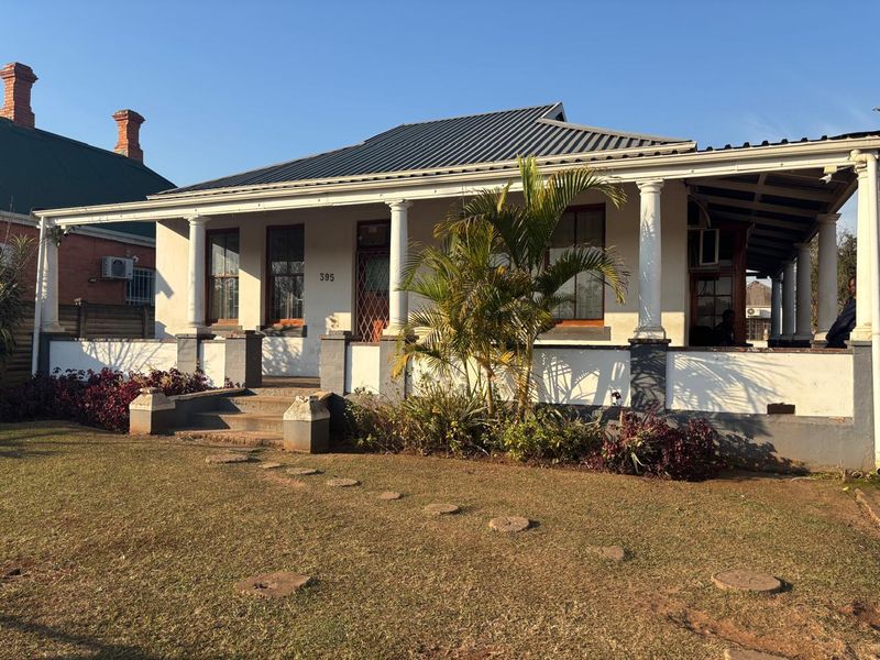 Front elevation of a classic office building featuring a covered veranda with columns, metal roofing, and a landscaped front garden area.
