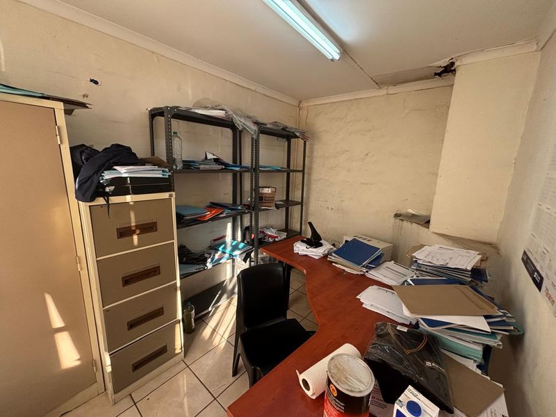A small office space featuring tiled flooring and fluorescent lighting, currently showing signs of wear including cracked plaster and damaged ceiling finishes.