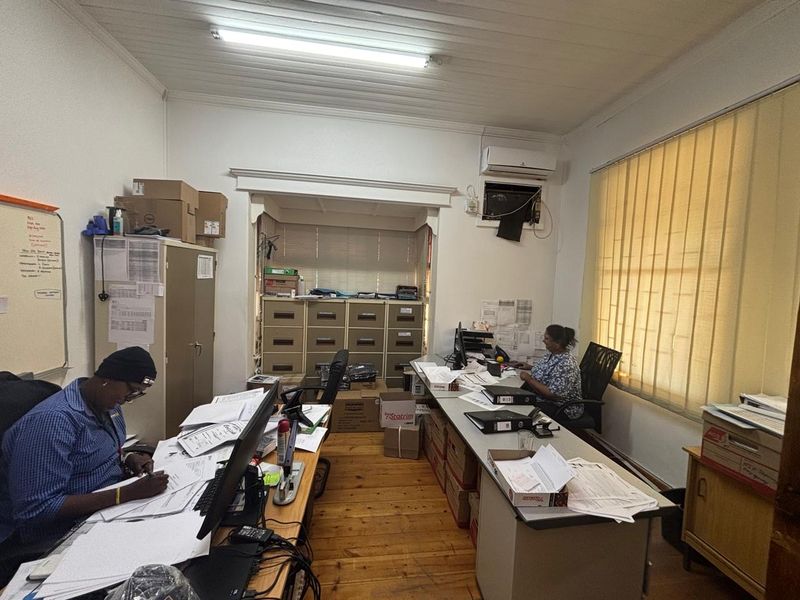 A functional office space featuring timber flooring, a timber-paneled ceiling, built-in filing storage, and a wall-mounted air conditioning unit.