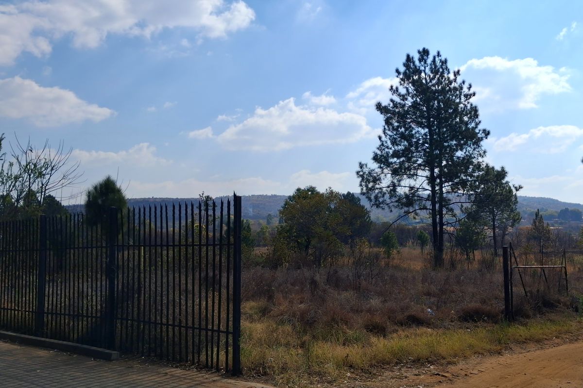 A view of a vacant commercial land plot featuring perimeter metal fencing and natural vegetation under a clear sky.