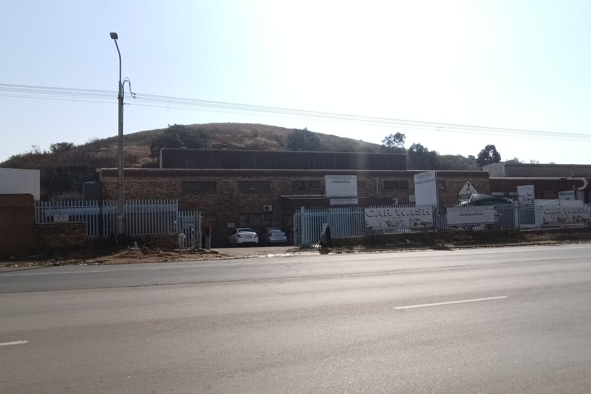 Street-facing view of an industrial property featuring a brick facade, secure perimeter fencing, and gated access points.