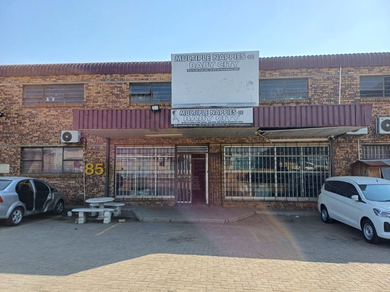 Front elevation of an industrial property featuring brick facade, security bars on windows, and dedicated parking space.