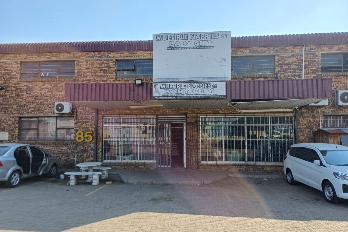 Front elevation of an industrial property featuring brick facade, security bars on windows, and dedicated parking space.