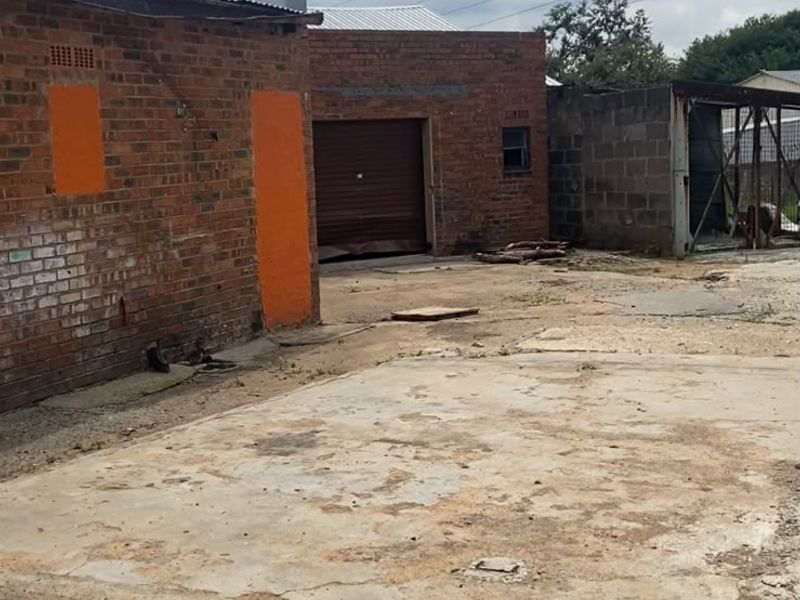 Rear industrial yard area featuring brick structures, a damaged roller shutter door, and a weathered concrete surface.