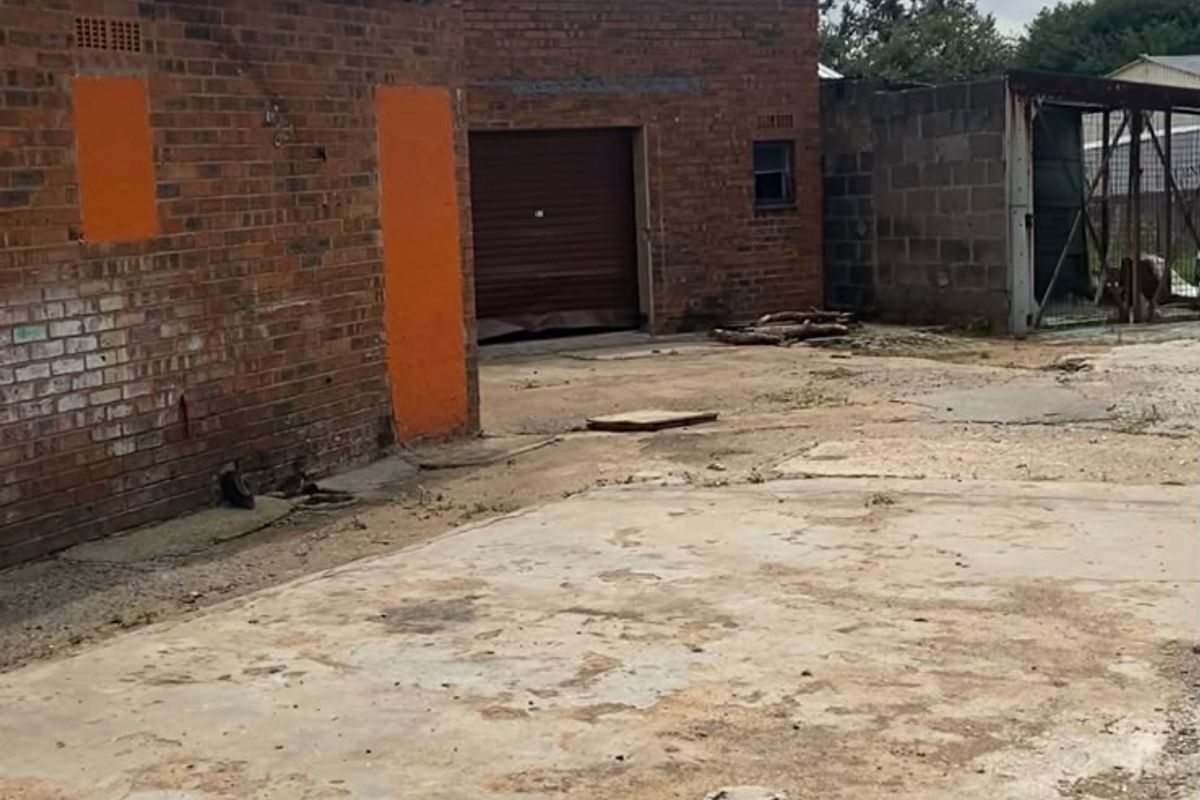 Rear industrial yard area featuring brick structures, a damaged roller shutter door, and a weathered concrete surface.