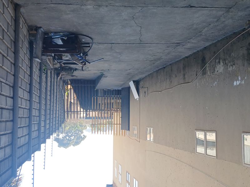 A side exterior passage of the industrial property featuring a concrete boundary wall with electric fencing and paved flooring.
