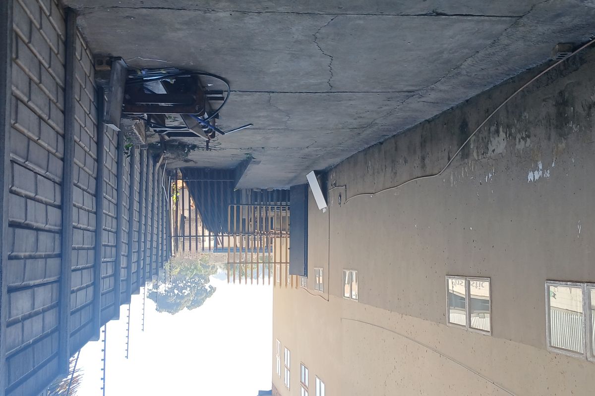A side exterior passage of the industrial property featuring a concrete boundary wall with electric fencing and paved flooring.