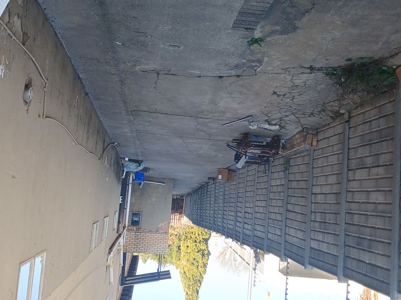 A narrow exterior side passage featuring a precast concrete boundary wall with electric fencing and weathered concrete paving.