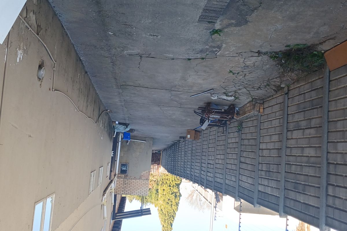 A narrow exterior side passage featuring a precast concrete boundary wall with electric fencing and weathered concrete paving.