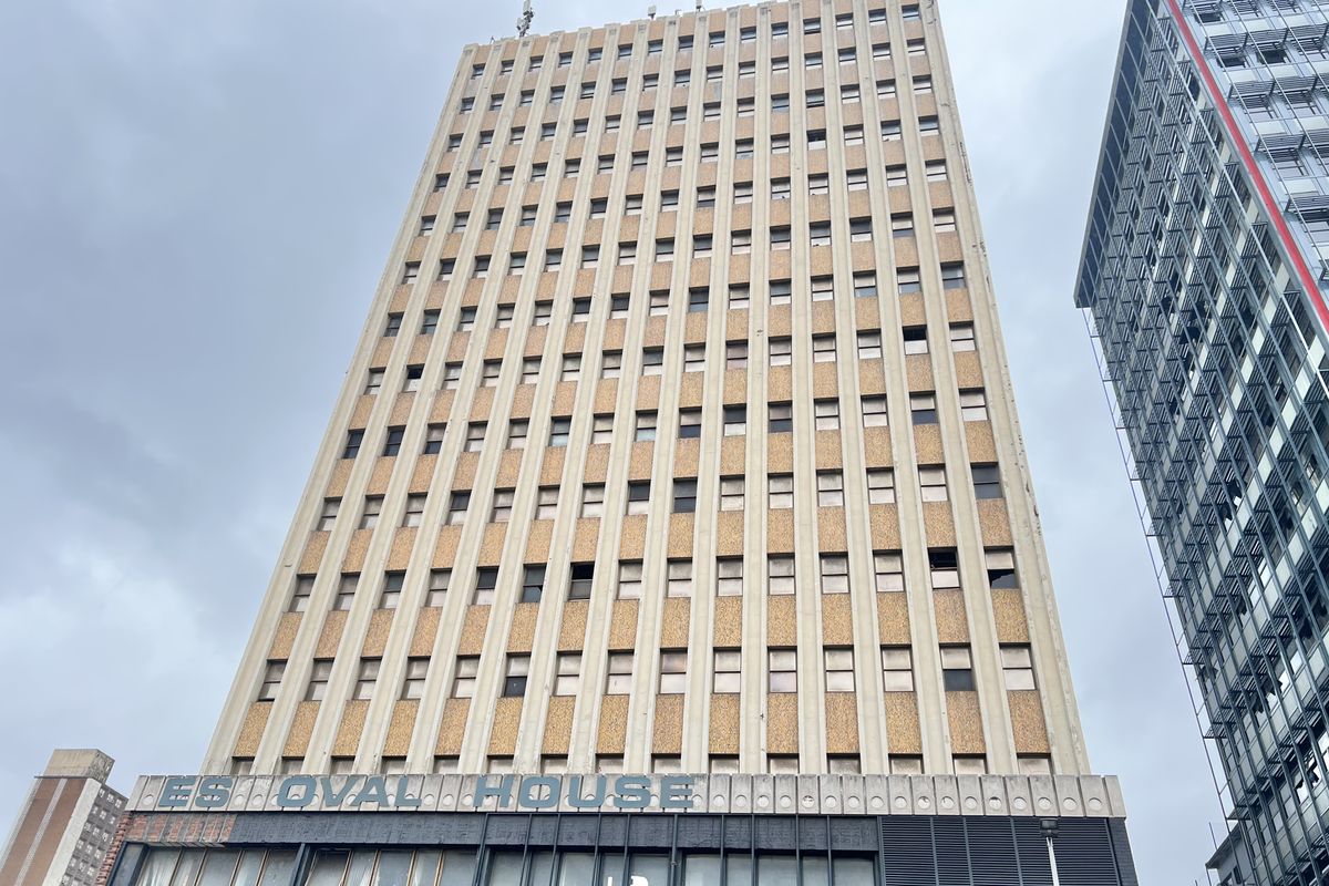 A low-angle exterior view of a multi-story high-rise building featuring a textured facade and prominent ground-level commercial signage.