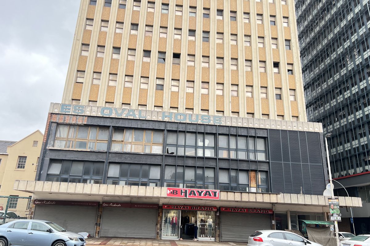 Exterior view of the multi-story Oval House building featuring ground-floor commercial retail spaces with roller shutter doors and large windows.