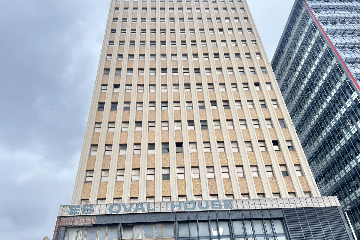 A low-angle view of a multi-story commercial apartment building featuring a concrete facade and ground-level storefront windows.