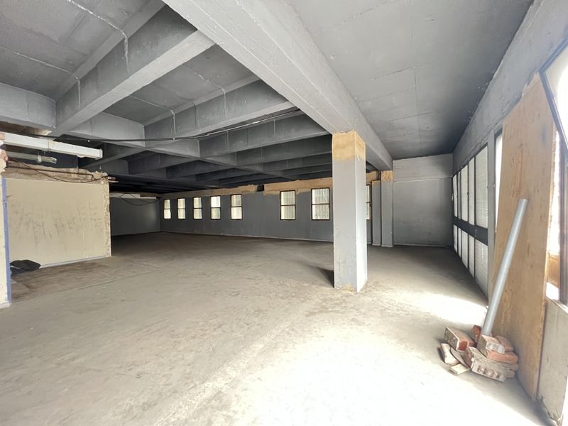 A large, open-plan interior space in shell condition, featuring exposed concrete ceilings, structural columns, and multiple windows, ready for a complete renovation.