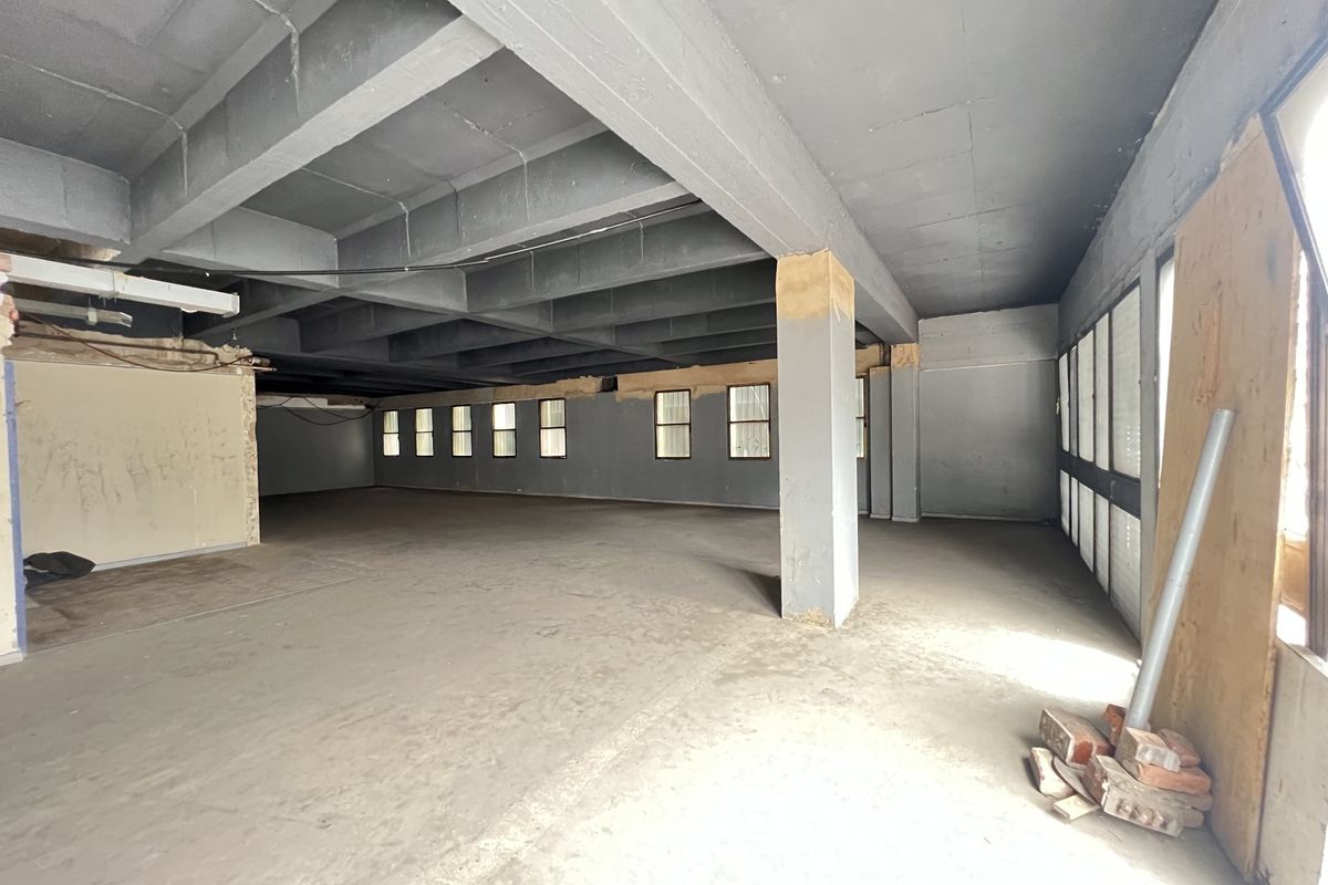 A large, open-plan interior space in shell condition, featuring exposed concrete ceilings, structural columns, and multiple windows, ready for a complete renovation.
