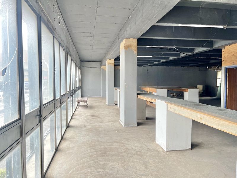 An expansive, industrial-style open-plan space featuring exposed concrete ceilings, structural columns, and large metal-framed windows, offering a blank canvas for renovation.