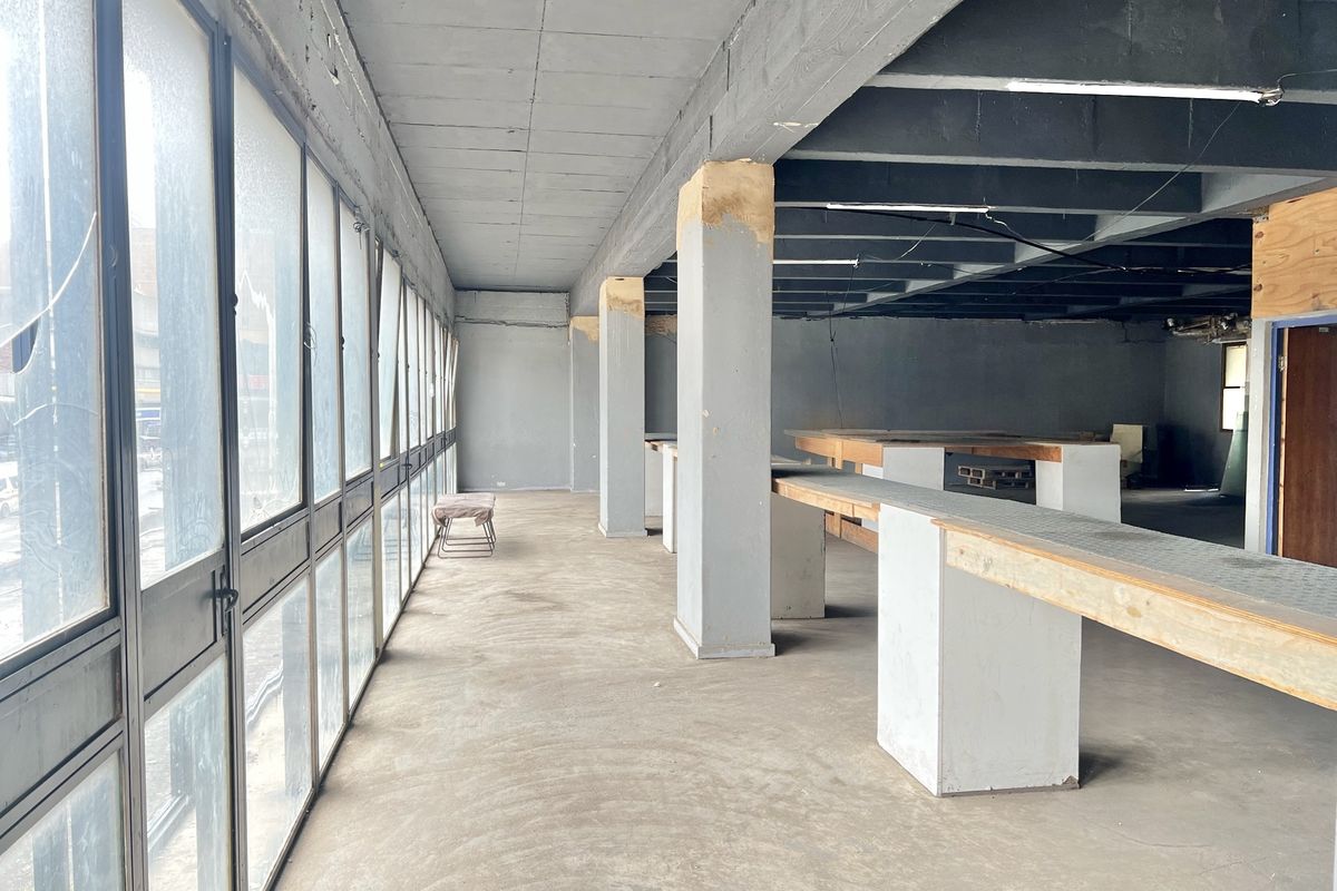 An expansive, industrial-style open-plan space featuring exposed concrete ceilings, structural columns, and large metal-framed windows, offering a blank canvas for renovation.