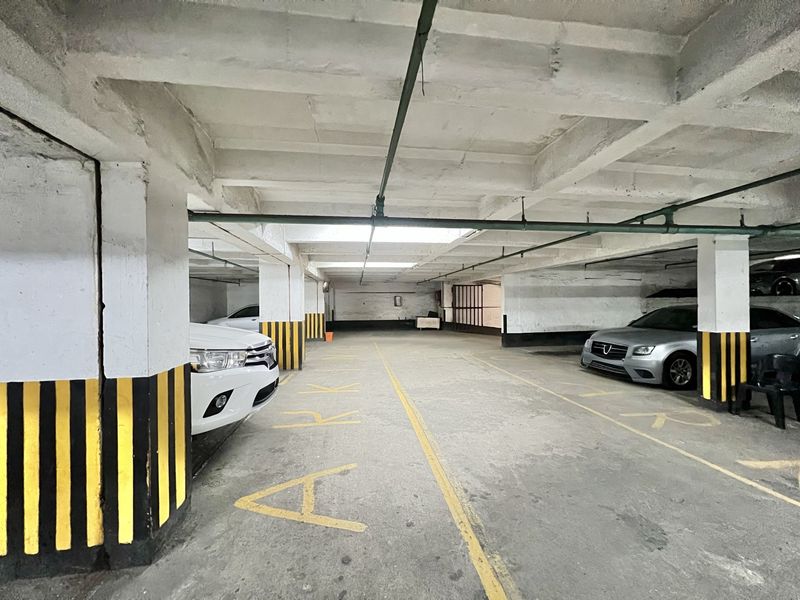 A covered basement parking garage featuring concrete structural elements, overhead piping, and designated parking bays with painted floor markings.
