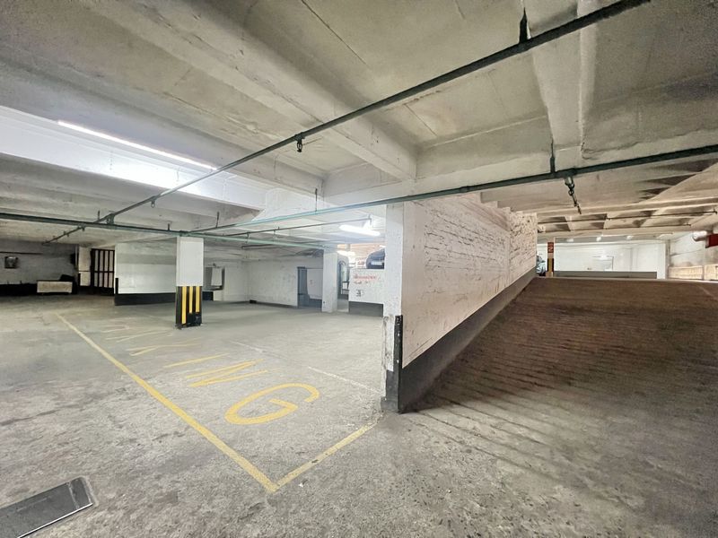 A spacious underground parking garage featuring a concrete ramp, overhead sprinkler system, and painted structural columns.