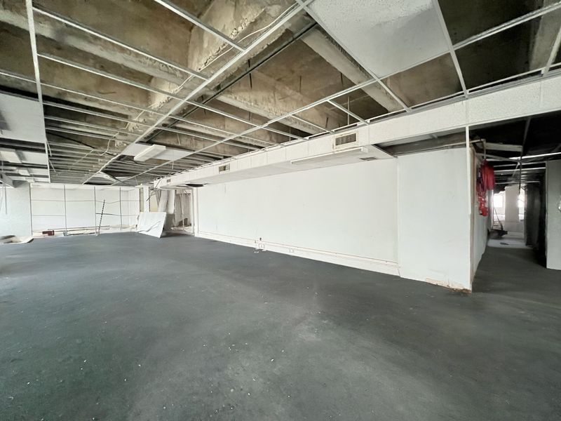 A large, vacant open-plan space currently in shell condition, featuring an exposed ceiling grid, ducted air conditioning, and carpeted flooring.