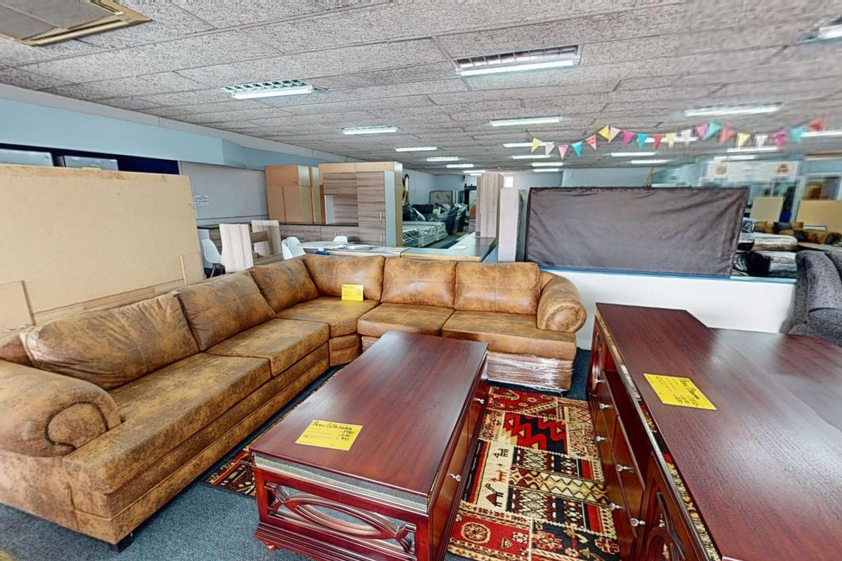 A commercial showroom space featuring a suspended ceiling with recessed lighting and carpeted flooring, currently utilized for furniture display.