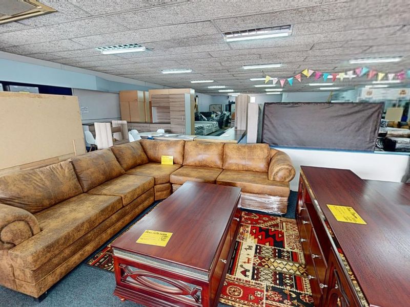 A commercial showroom space featuring a suspended ceiling with recessed lighting and carpeted flooring, currently utilized for furniture display.