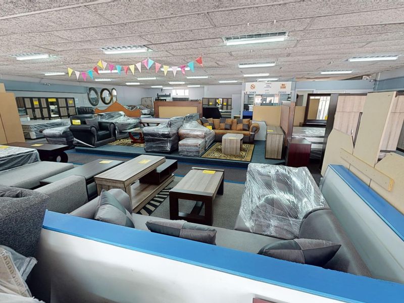 A large open-plan commercial showroom space featuring suspended acoustic ceiling tiles and recessed fluorescent lighting, currently utilized for furniture retail display.