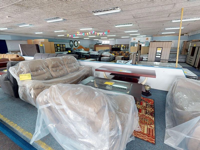 A large open-plan commercial showroom space featuring suspended acoustic ceiling tiles, fluorescent lighting, and carpeted flooring throughout.