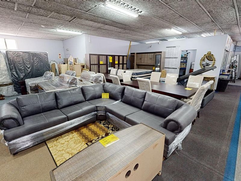 A large open-plan commercial showroom space featuring acoustic ceiling tiles and overhead fluorescent lighting, currently utilized for furniture retail display.
