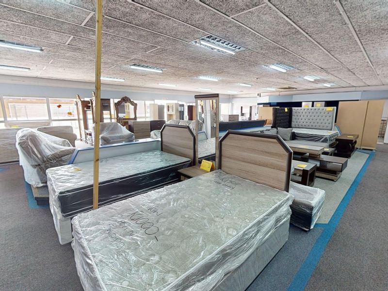 A commercial showroom space featuring suspended acoustic ceiling tiles, recessed fluorescent lighting, and carpeted flooring, currently utilized for furniture display.