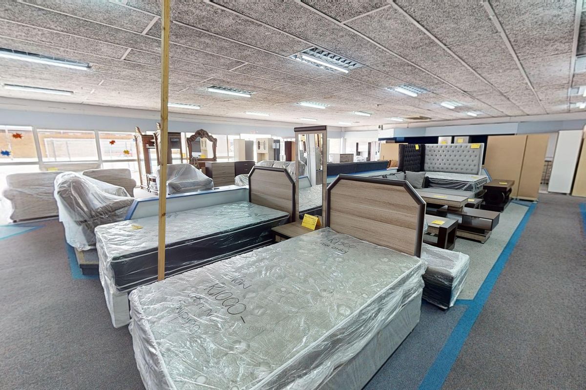 A commercial showroom space featuring suspended acoustic ceiling tiles, recessed fluorescent lighting, and carpeted flooring, currently utilized for furniture display.