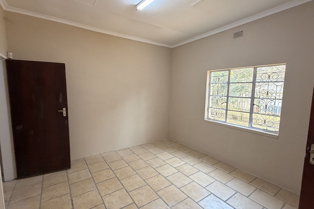 A vacant bedroom featuring neutral wall tones, tiled flooring, and a window fitted with security bars.
