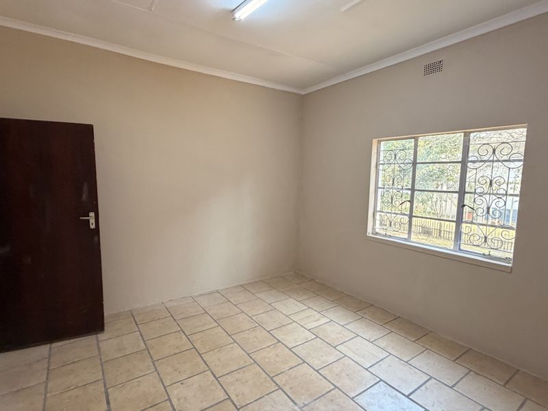 A vacant bedroom featuring neutral wall tones, tiled flooring, and a window fitted with security bars.