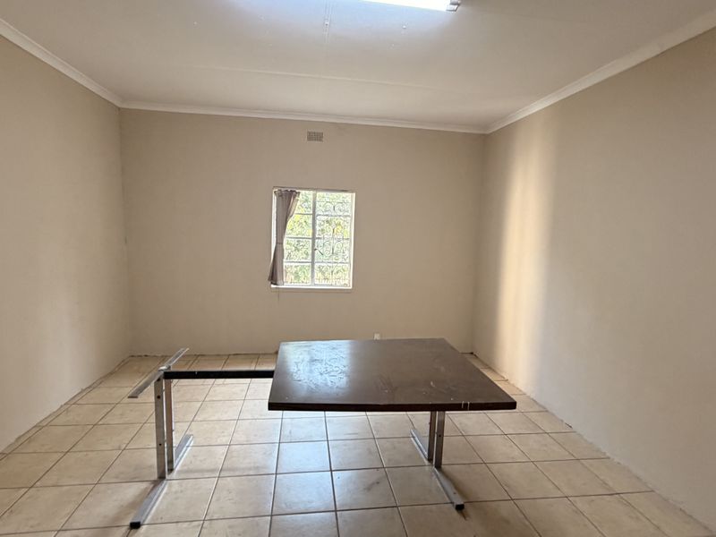 A vacant office space featuring neutral wall tones, ceramic tiled flooring, and a window fitted with security bars.