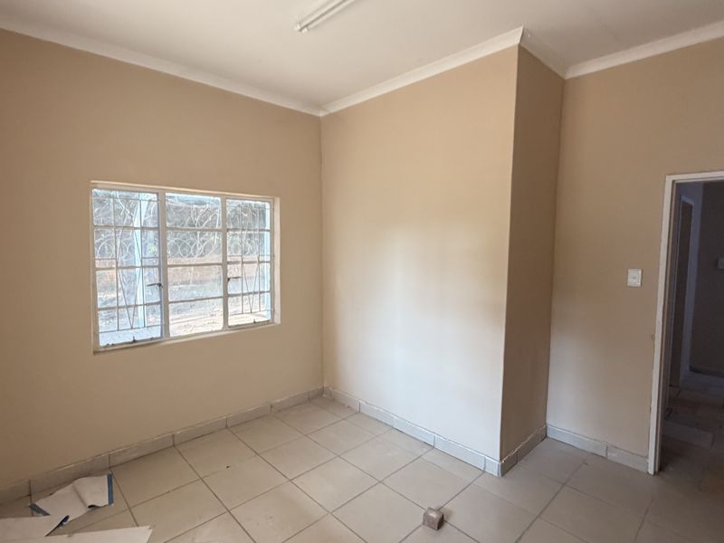 An empty bedroom featuring tiled flooring, security bars on the window, and neutral wall paint, offering a blank canvas for potential occupants.