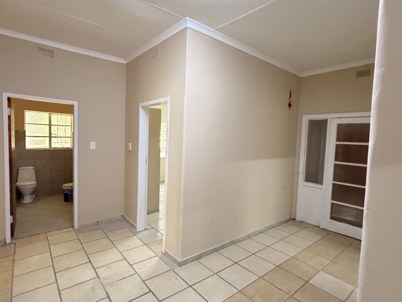 A vacant hallway featuring tiled flooring, cornicing, and access to adjacent rooms, including a bathroom with a visible toilet.