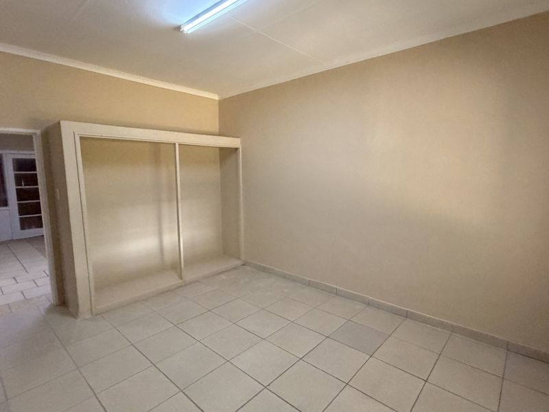 An empty bedroom featuring tiled flooring, a built-in shelving unit, and neutral wall tones, offering a blank canvas for potential occupants.