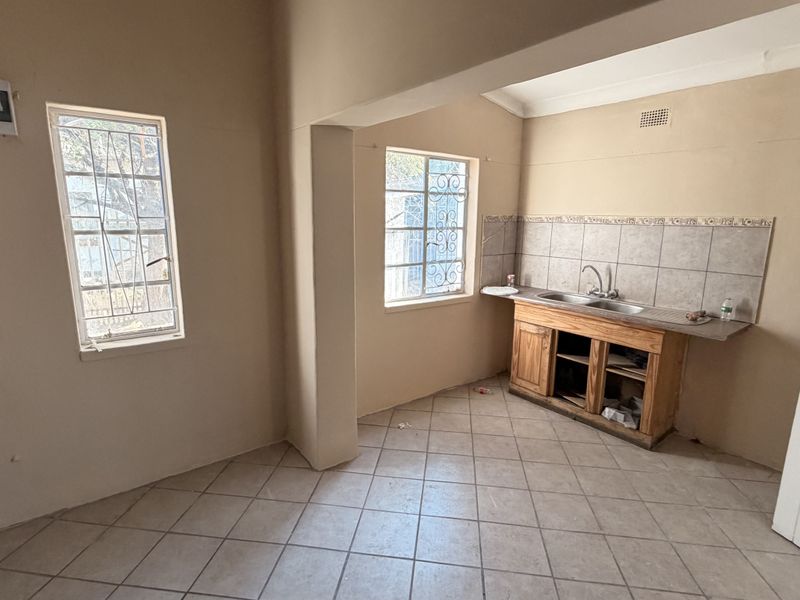 A vacant kitchen area featuring a double sink, tiled splashback, and wooden base cabinetry, requiring cosmetic updates and repairs to the cabinetry.
