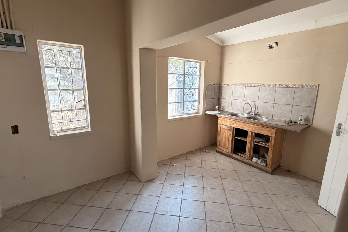 A vacant kitchen area featuring a double sink, tiled splashback, and wooden base cabinetry, requiring cosmetic updates and repairs to the cabinetry.