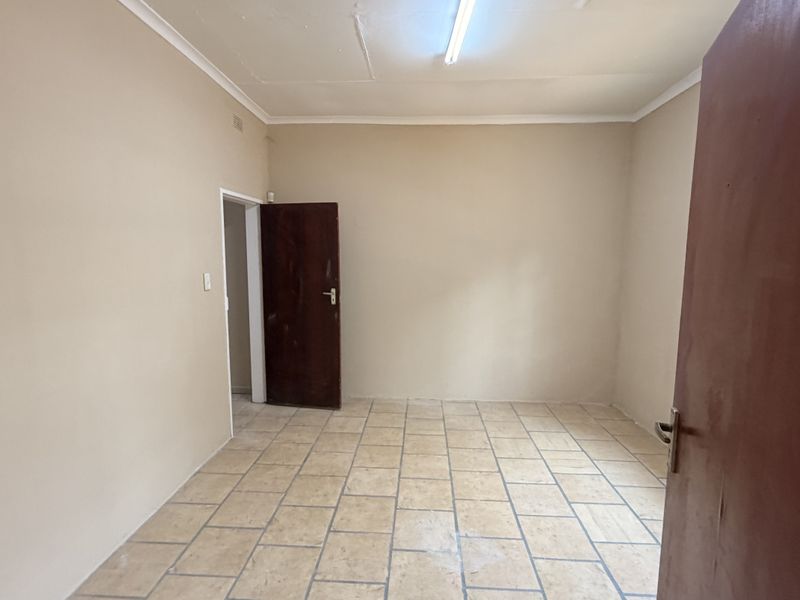 An empty, functional office space featuring tiled flooring, neutral wall paint, and a standard timber door, suitable for various commercial uses.