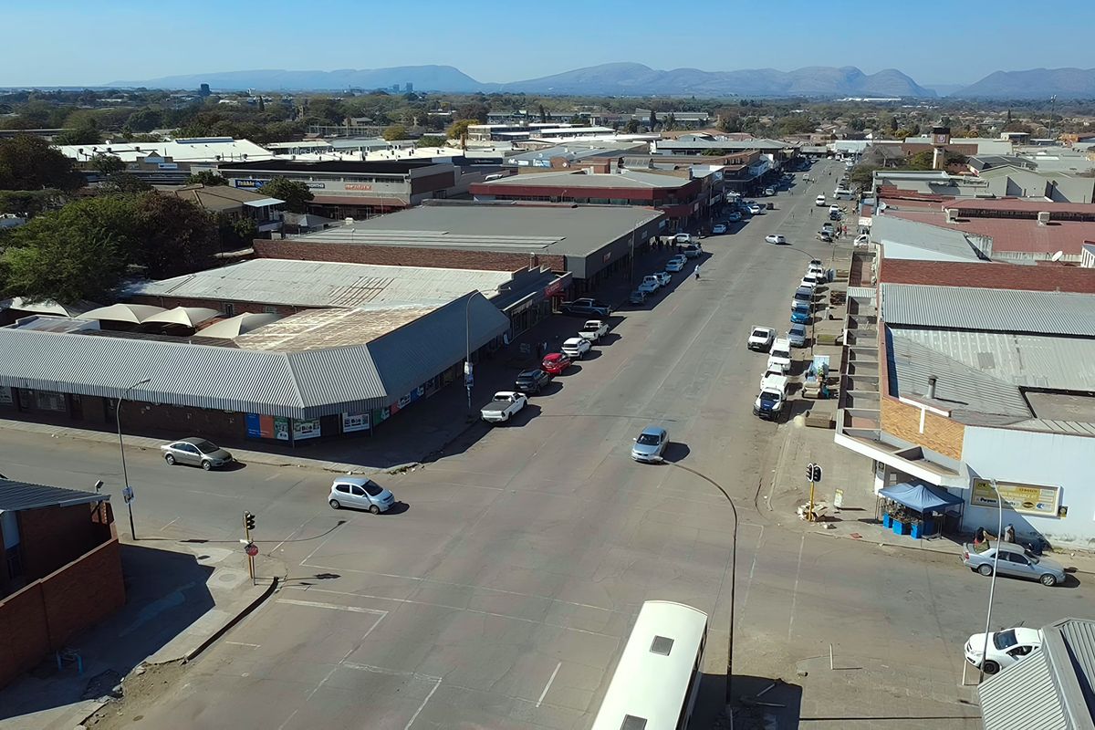 Aerial view of a commercial street intersection featuring various retail buildings with metal roofing and surrounding urban infrastructure.